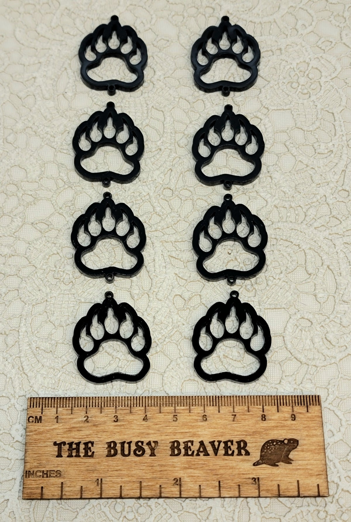 Two sets of four graduated acrylic open bear paws in black, beside a ruler