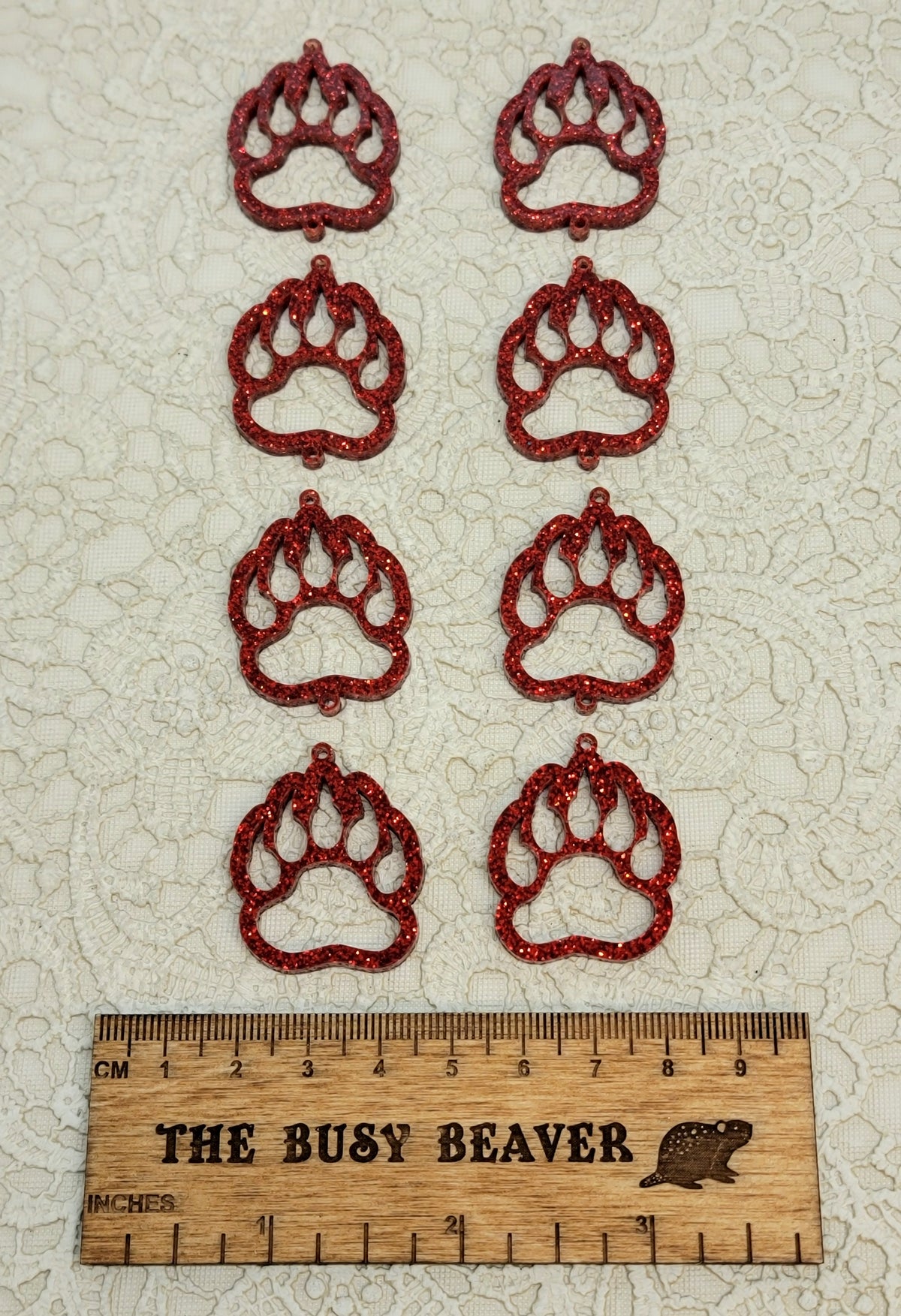 Two sets of four graduated acrylic open bear paws in red glitter, beside a ruler