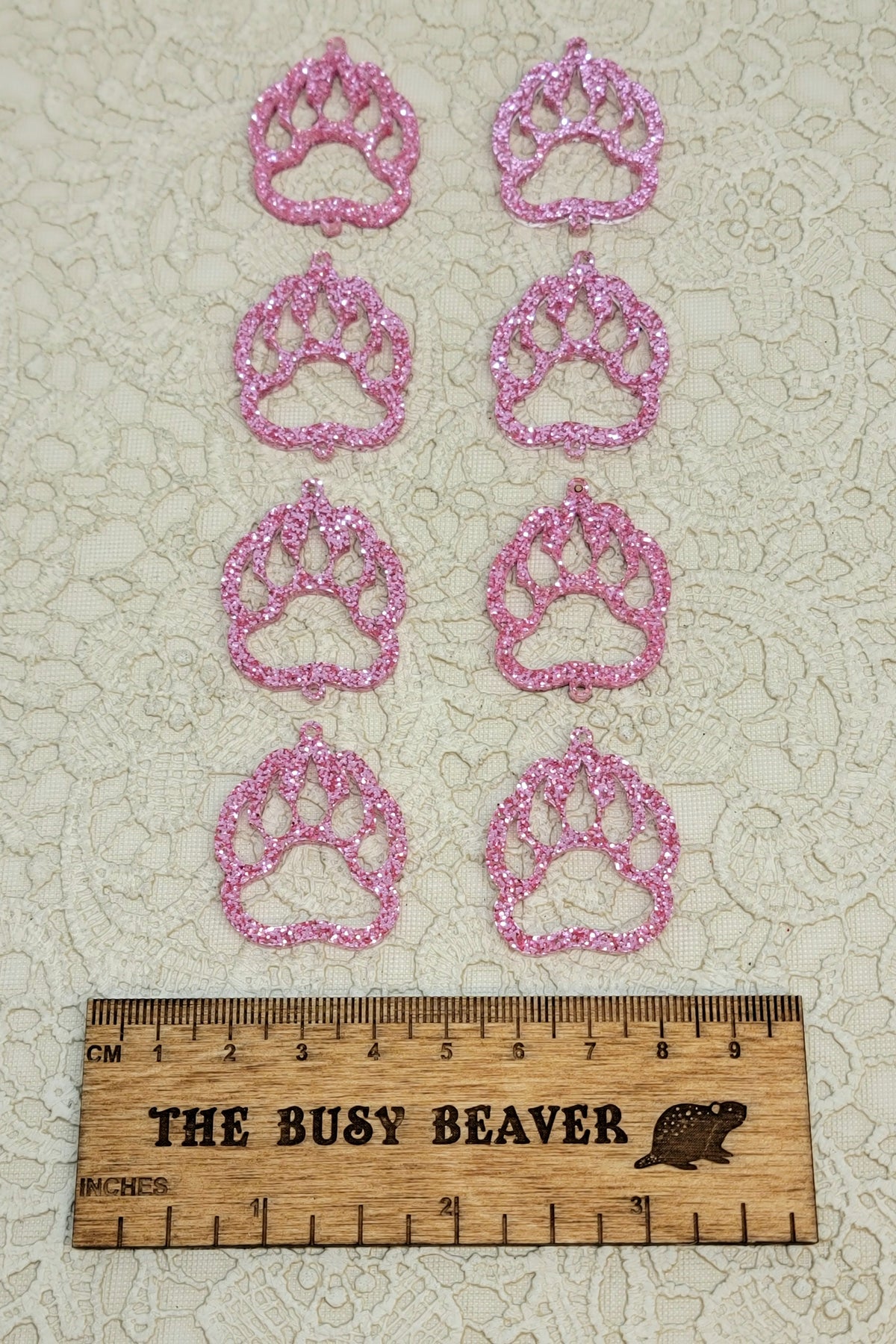 Two sets of four graduated acrylic open bear paws in pink glitter, beside a ruler