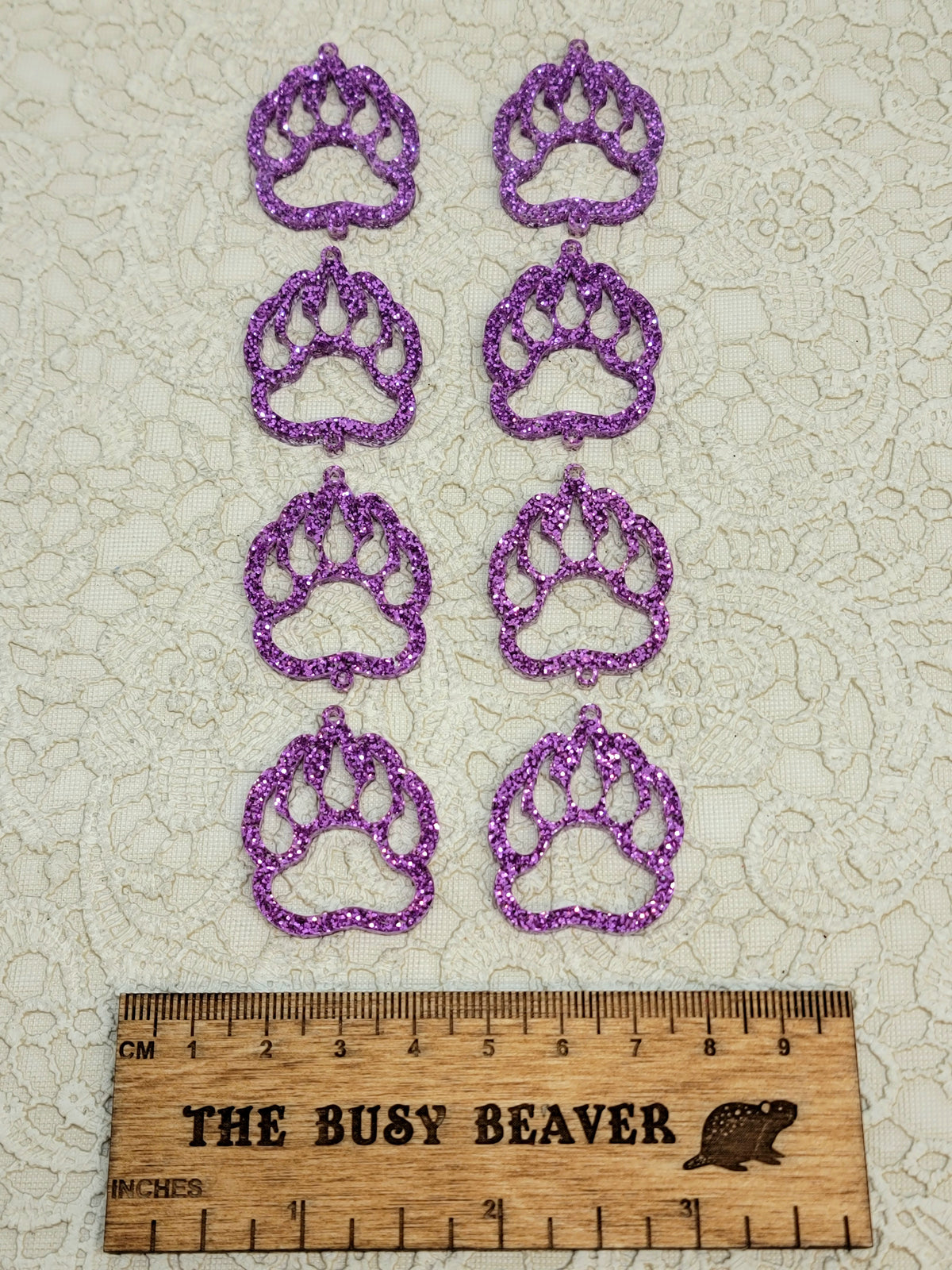 Two sets of four graduated acrylic open bear paws in purple glitter, beside a ruler