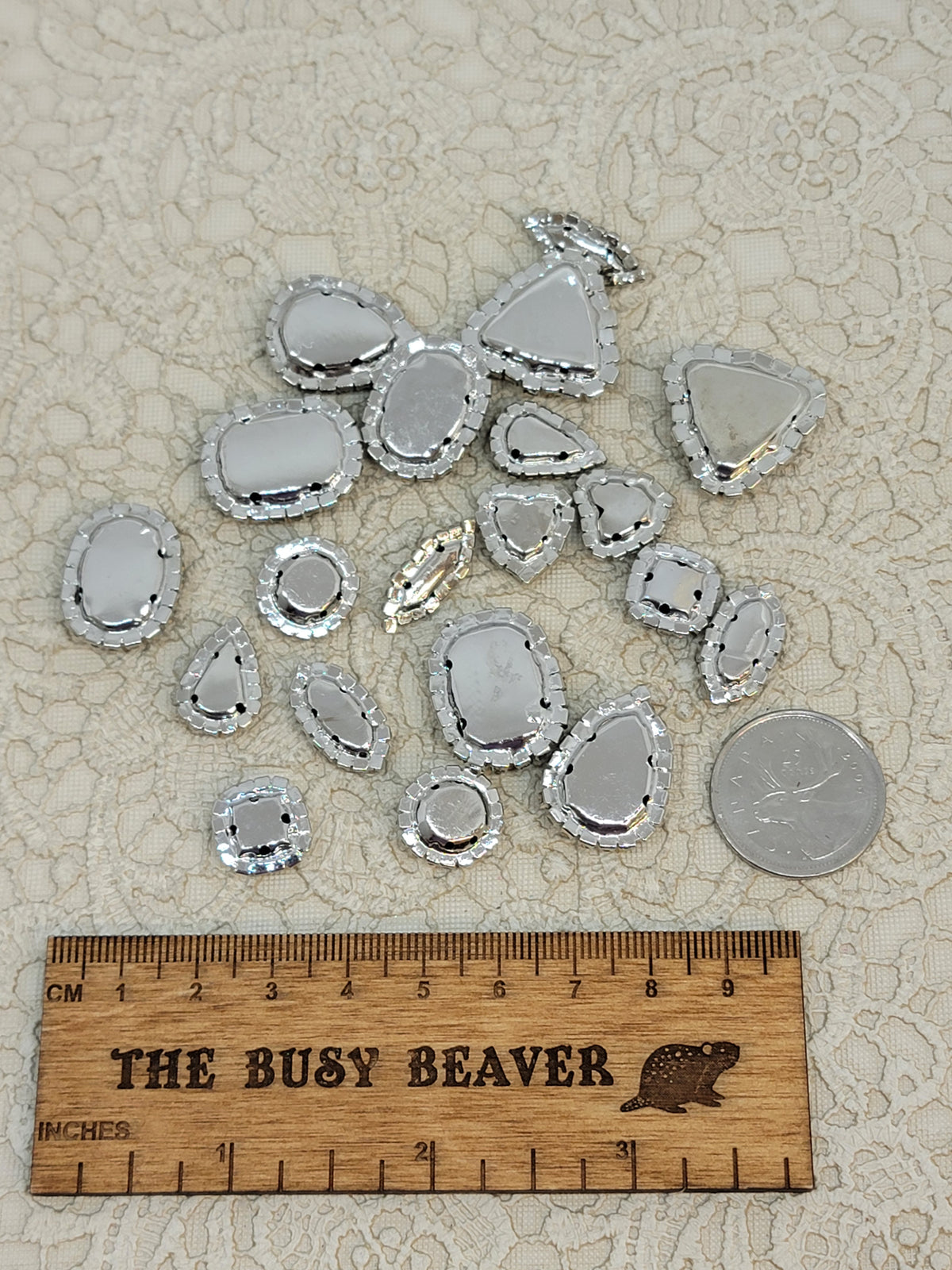 Back view of sew-on rhinestones in silver claw settings with sew-through holes, beside a ruler