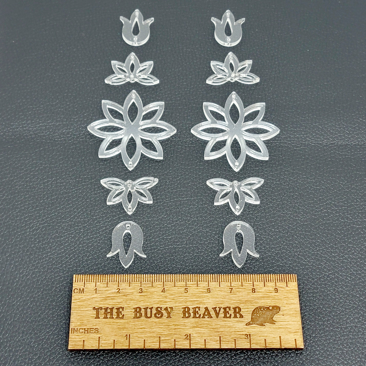 Two 5-tier acrylic flower earring sets in clear, laid out top to bottom beside a ruler