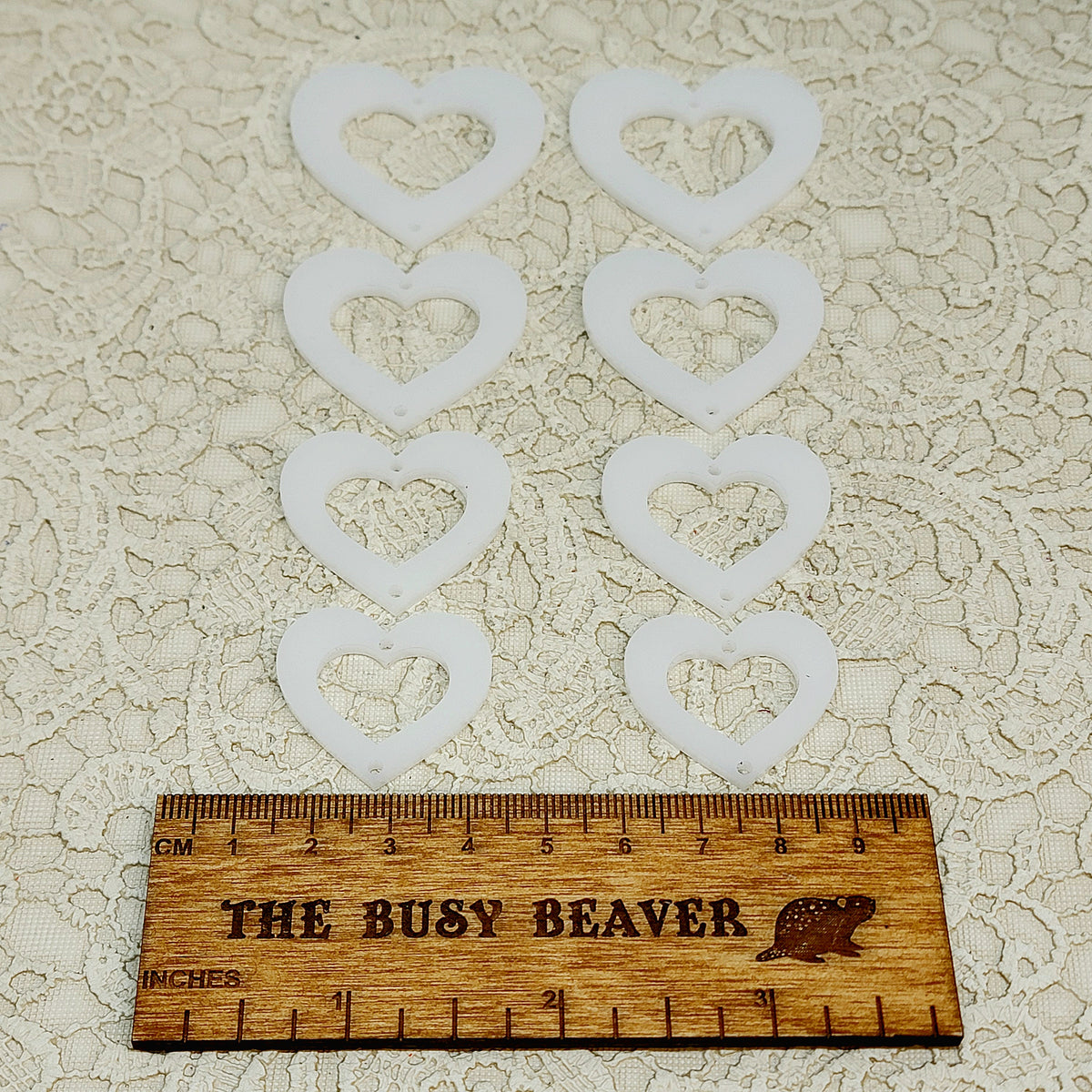 Two sets of four graduated acrylic open hearts in linen, beside a ruler