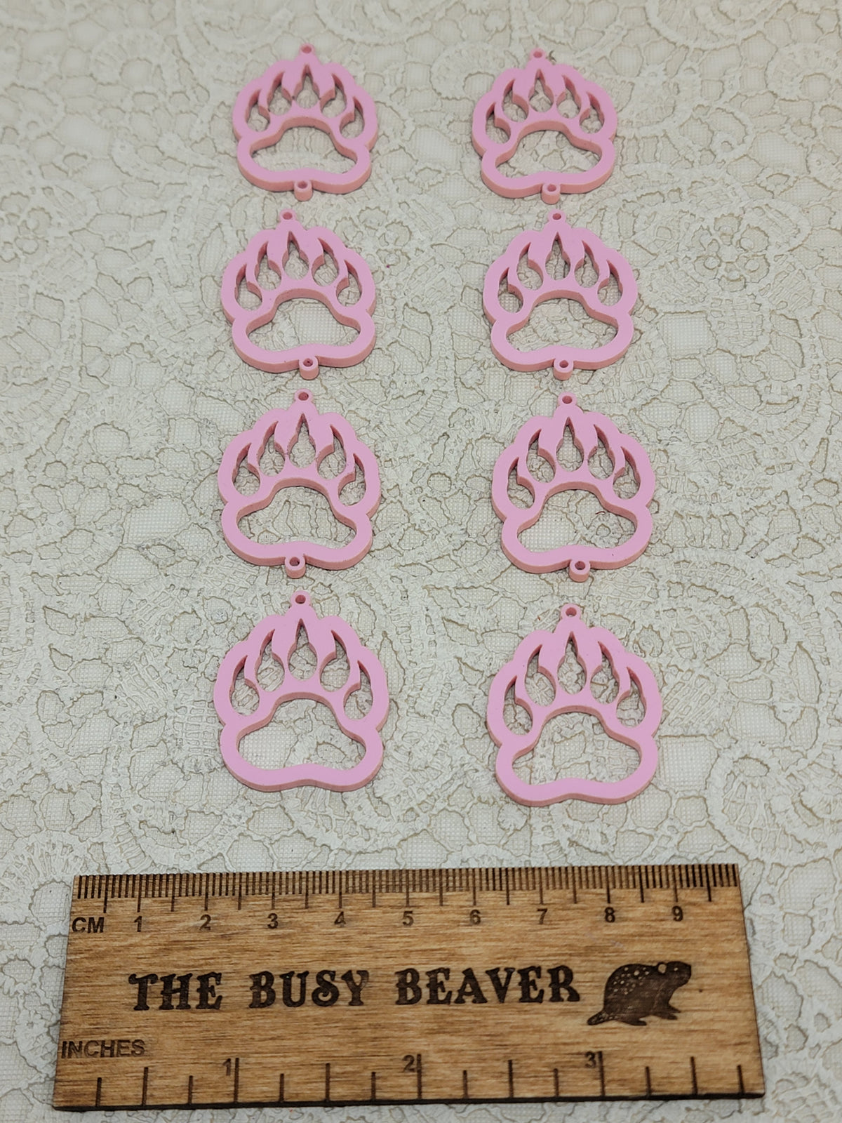 Two sets of four graduated acrylic open bear paws in pastel pink, beside a ruler