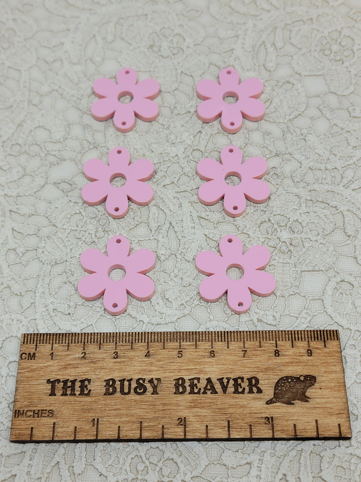 Two sets of three graduated acrylic flower pieces in pastel pink, beside a ruler