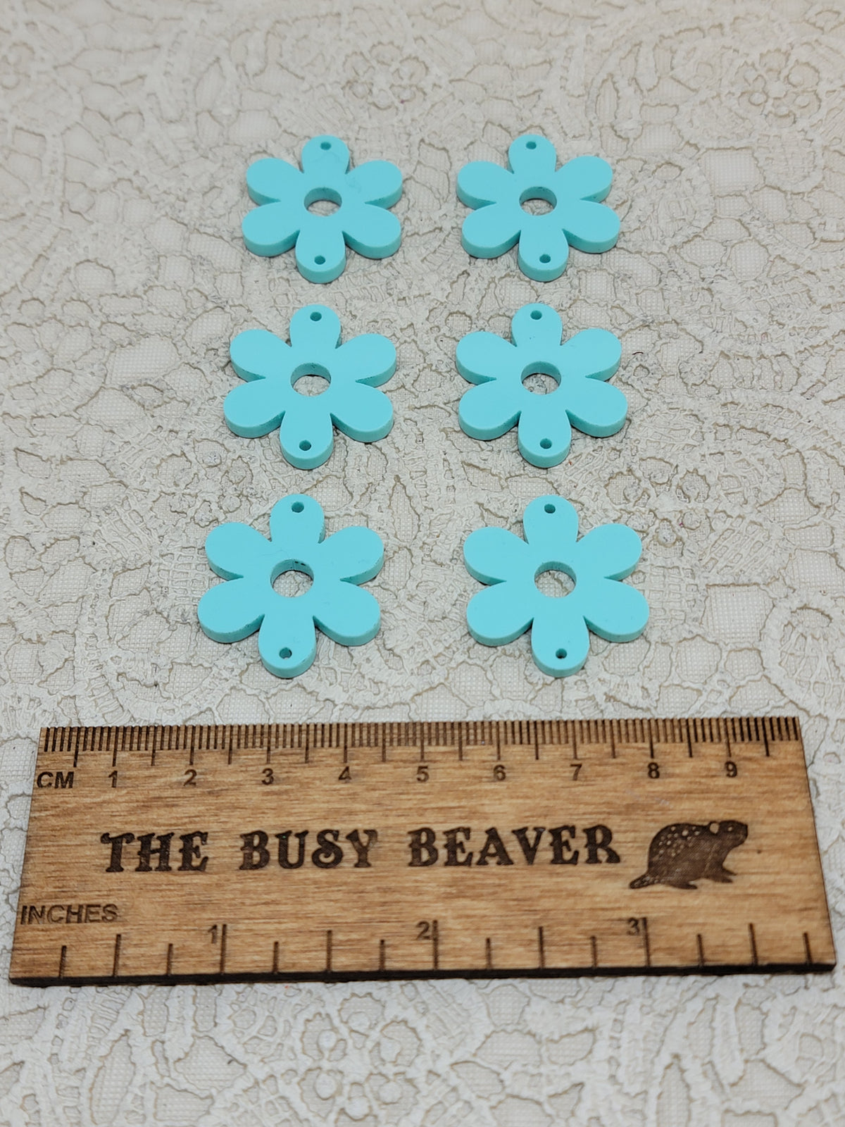 Two sets of three graduated acrylic flower pieces in pastel turquoise, beside a ruler