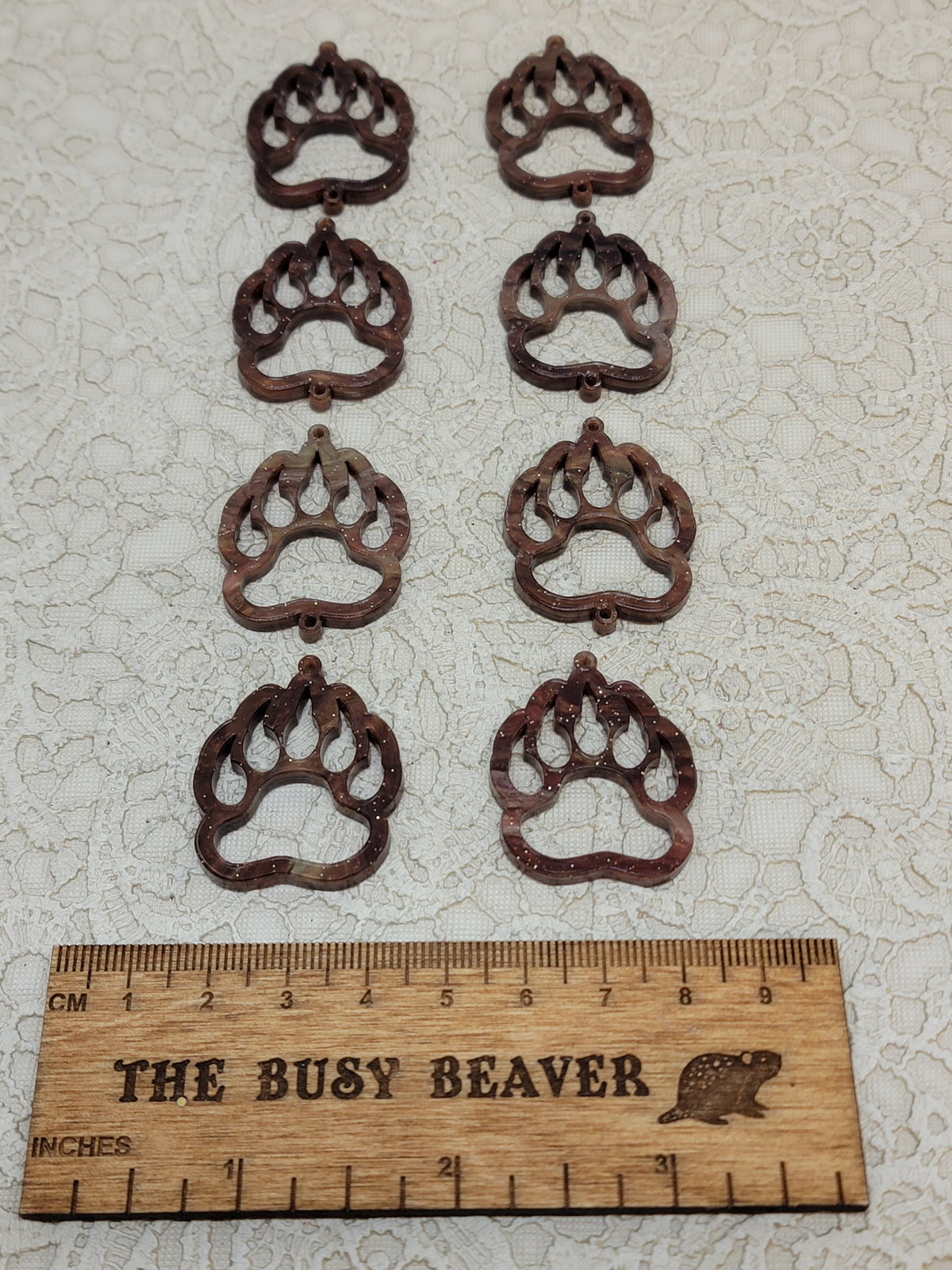 Two sets of four graduated acrylic open bear paws in brown marble, beside a ruler