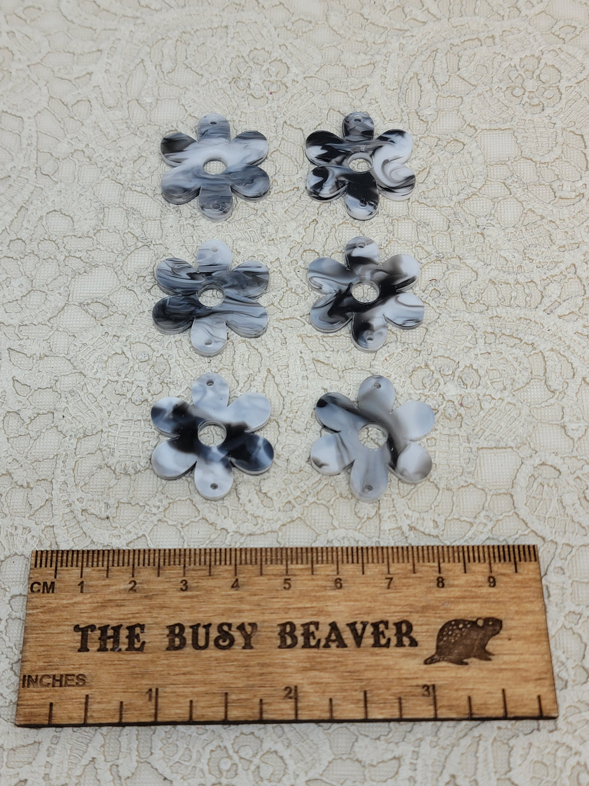 Two sets of three graduated acrylic flower pieces in black/white marble, beside a ruler