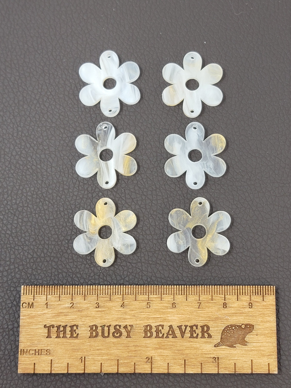 Two sets of three graduated acrylic flower pieces in gold/white marble, beside a ruler