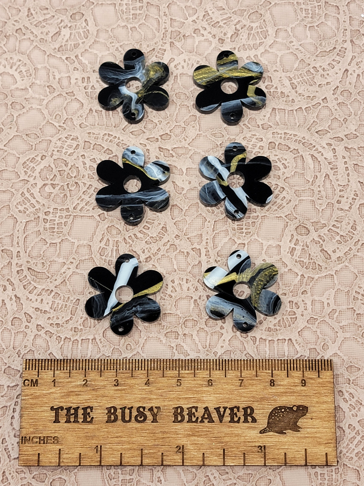Two sets of three graduated acrylic flower pieces in black/gold/white marble, beside a ruler