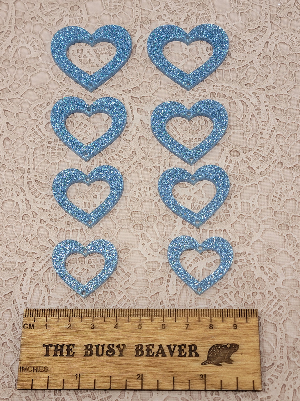 Two sets of four graduated acrylic open hearts in light blue sparkle, beside a ruler