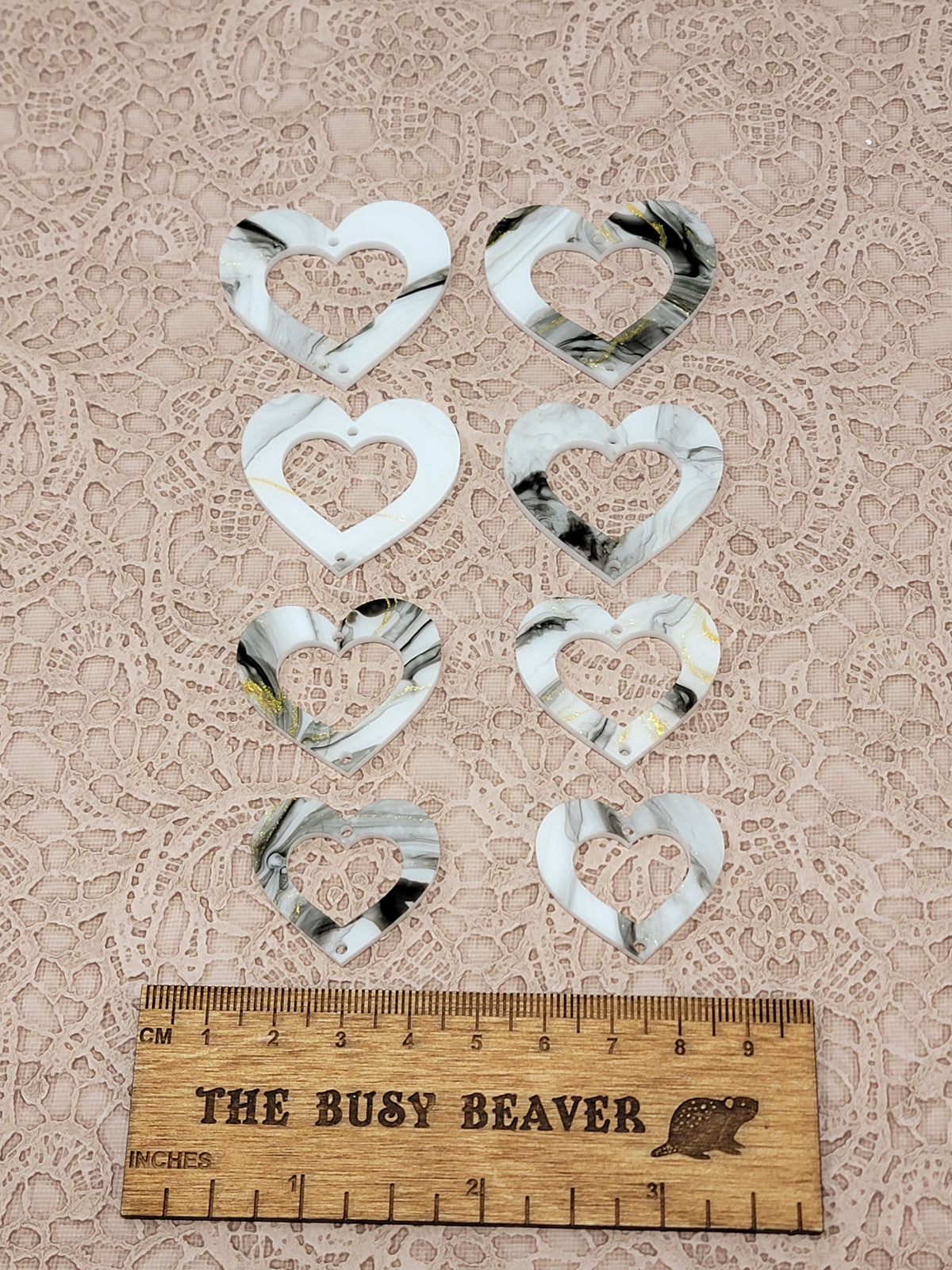 Two sets of four graduated acrylic open hearts in white/black/gold marble, beside a ruler