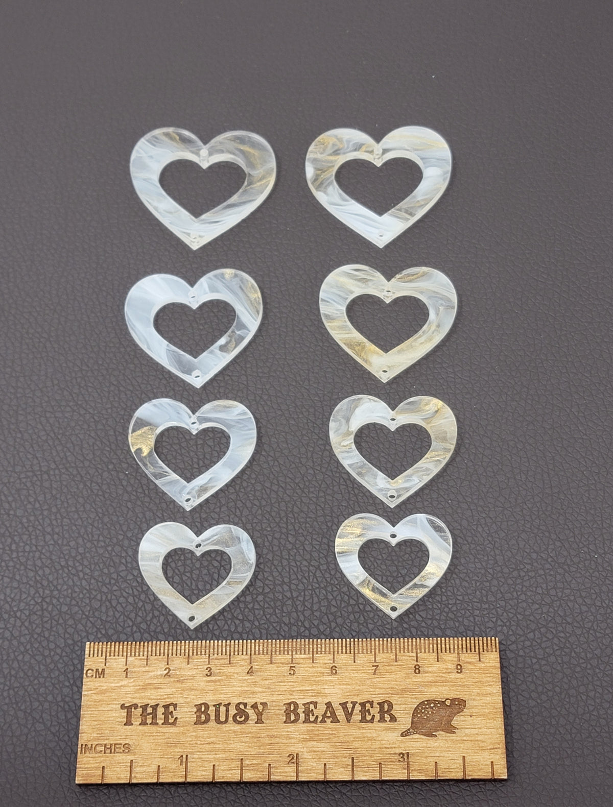 Two sets of four graduated acrylic open hearts in white/gold marble, beside a ruler