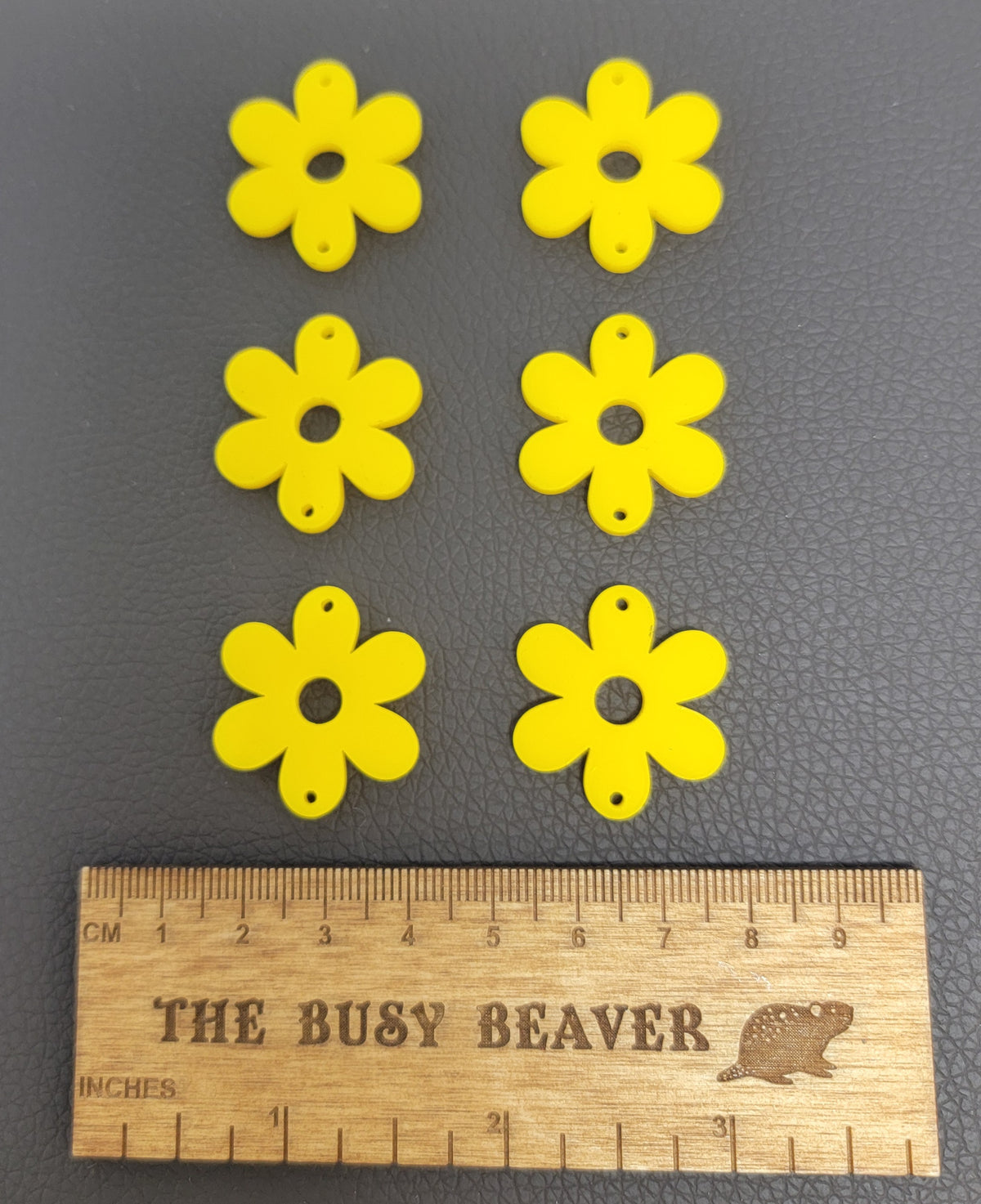 Two sets of three graduated acrylic flower pieces in yellow, beside a ruler