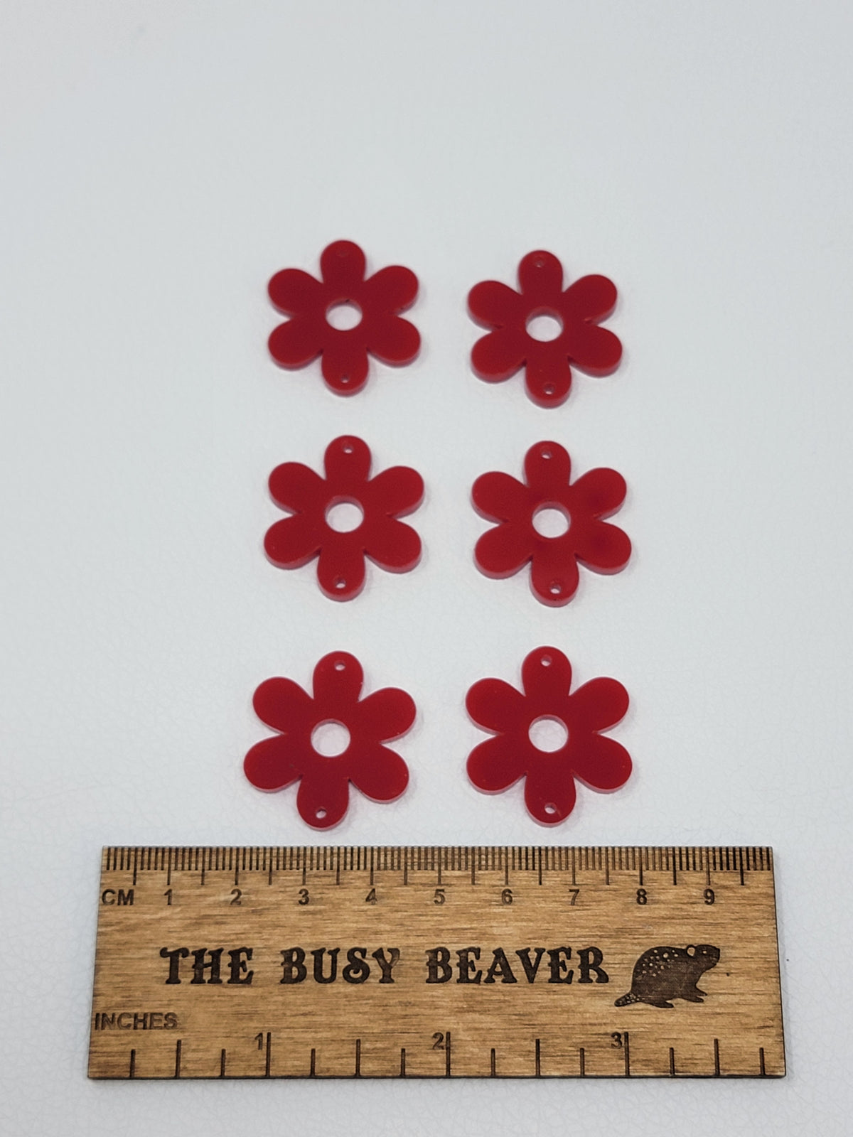 Two sets of three graduated acrylic flower pieces in red, beside a ruler
