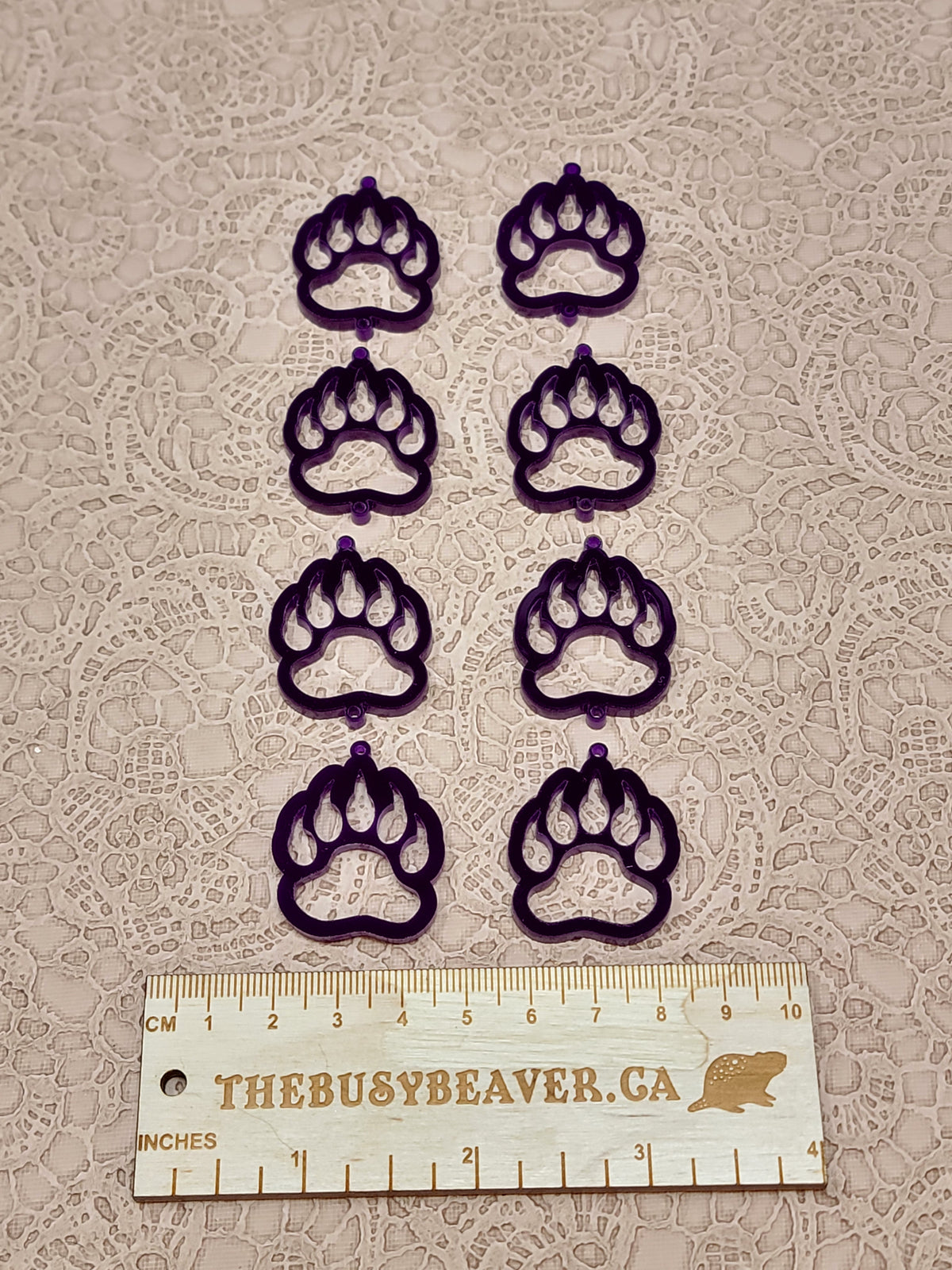 Two sets of four graduated acrylic open bear paws in dark purple, beside a ruler