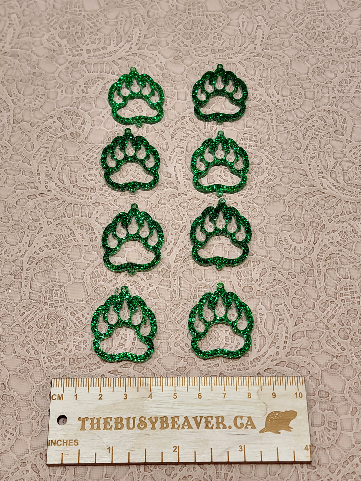 Two sets of four graduated acrylic open bear paws in green glitter, beside a ruler