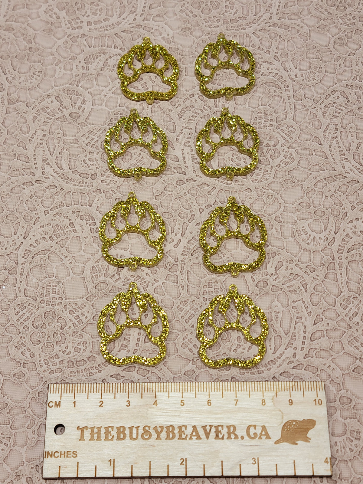 Two sets of four graduated acrylic open bear paws in gold glitter, beside a ruler
