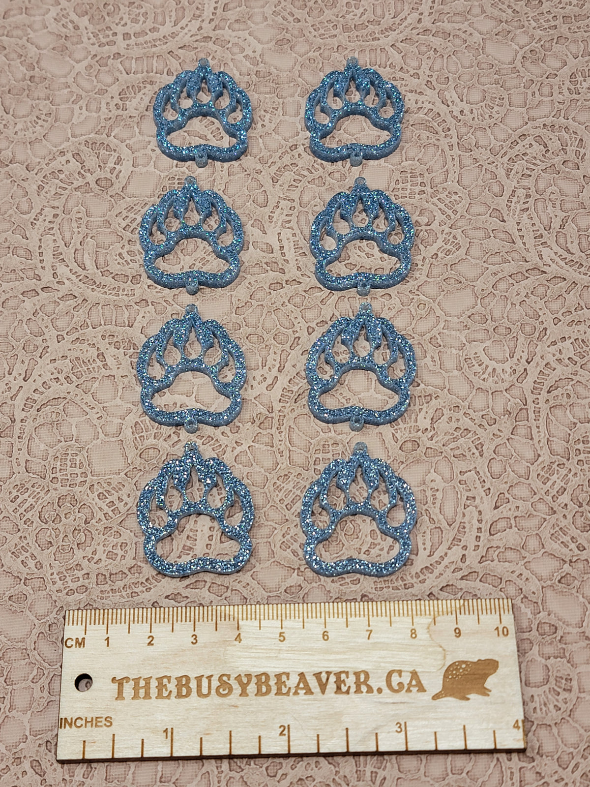 Two sets of four graduated acrylic open bear paws in light blue glitter, beside a ruler