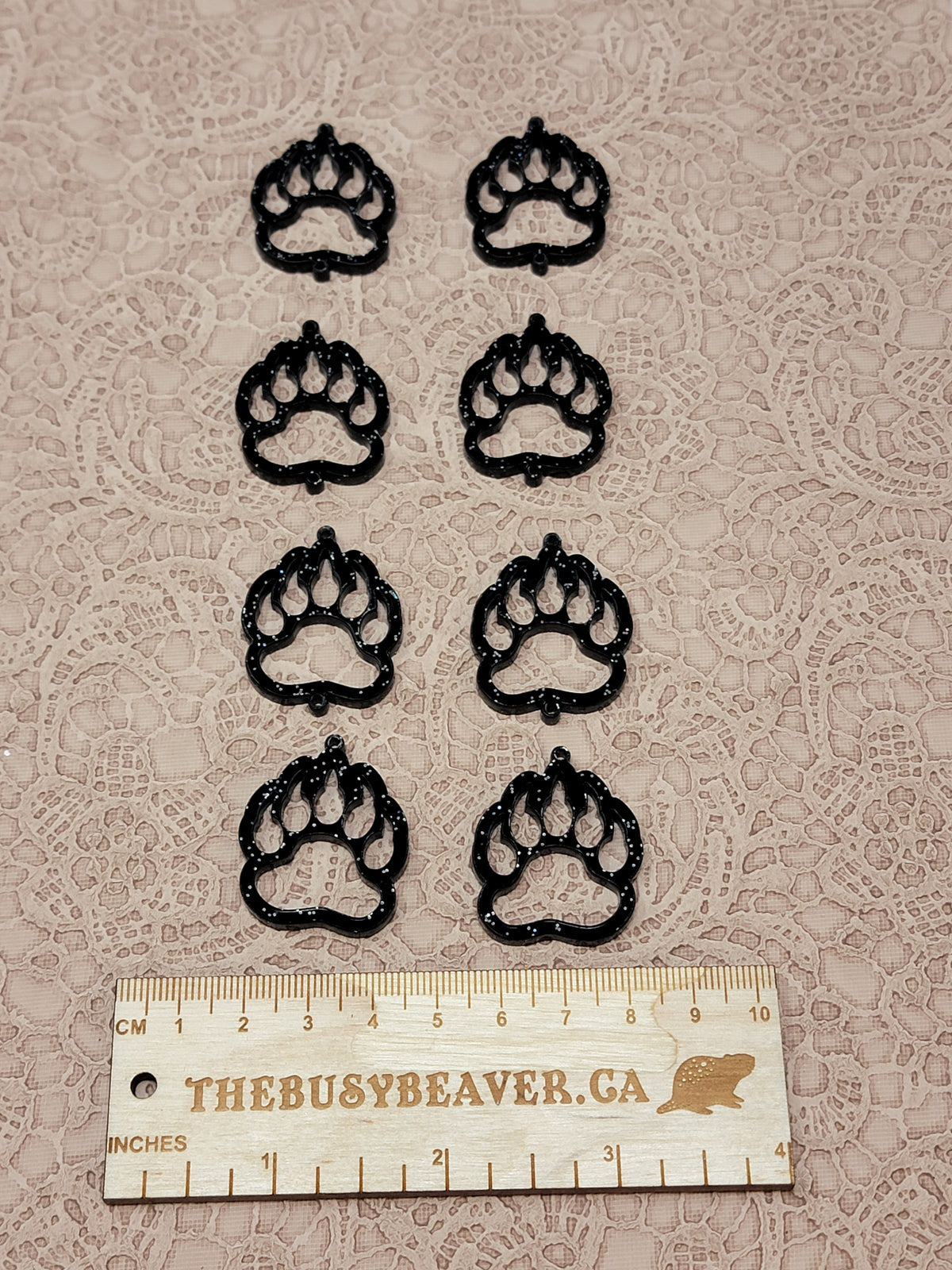 Two sets of four graduated acrylic open bear paws in black glitter, beside a ruler