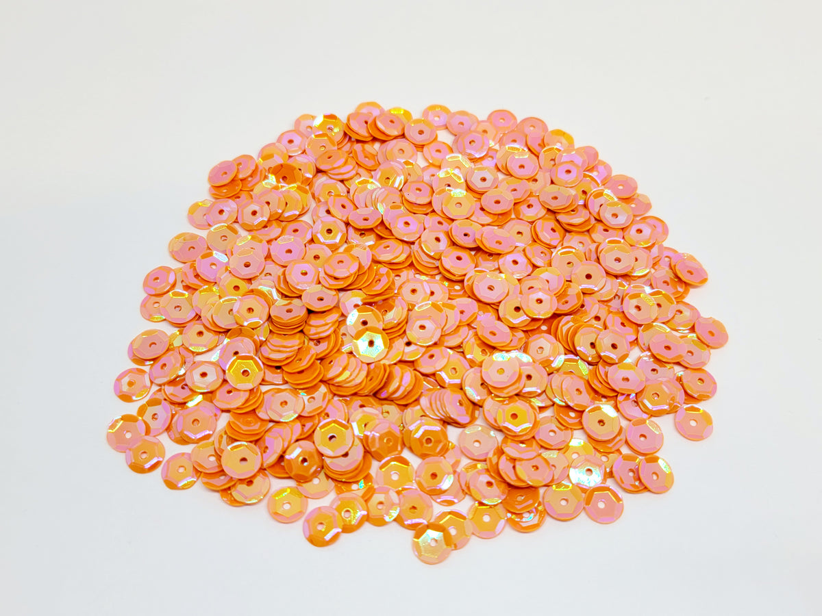 Pile of 6mm round orange sequins with centre holes, on a white background