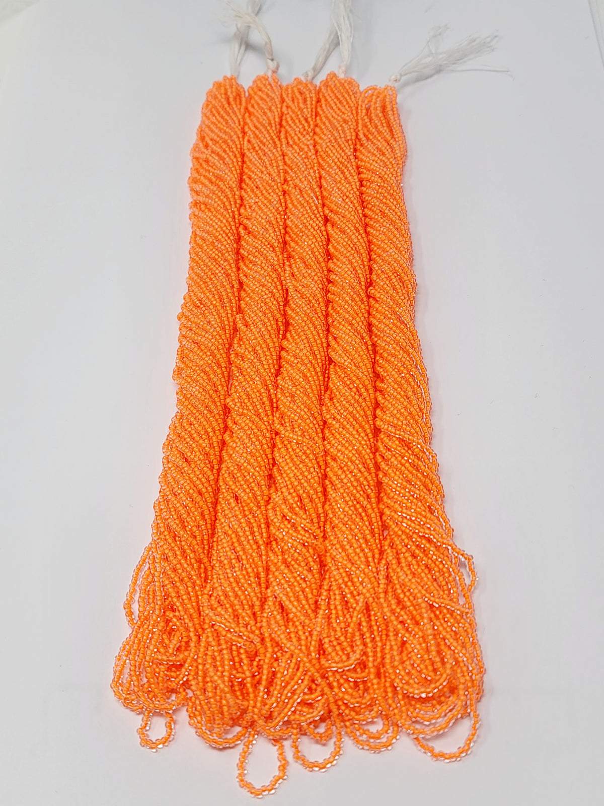 Five hanks of Preciosa 11/0 transparent neon orange seed beads laid out on a white background