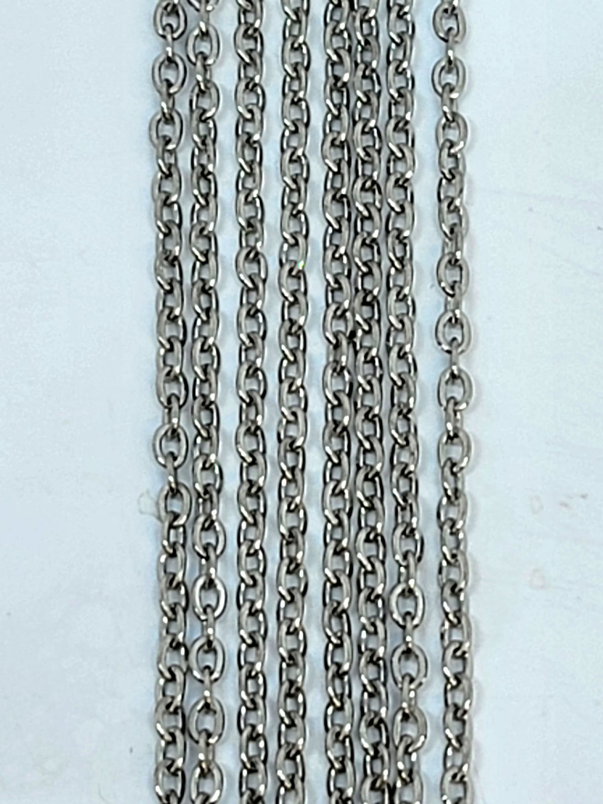 Hanging strands of 2mm rhodium stainless steel link chain against a white background