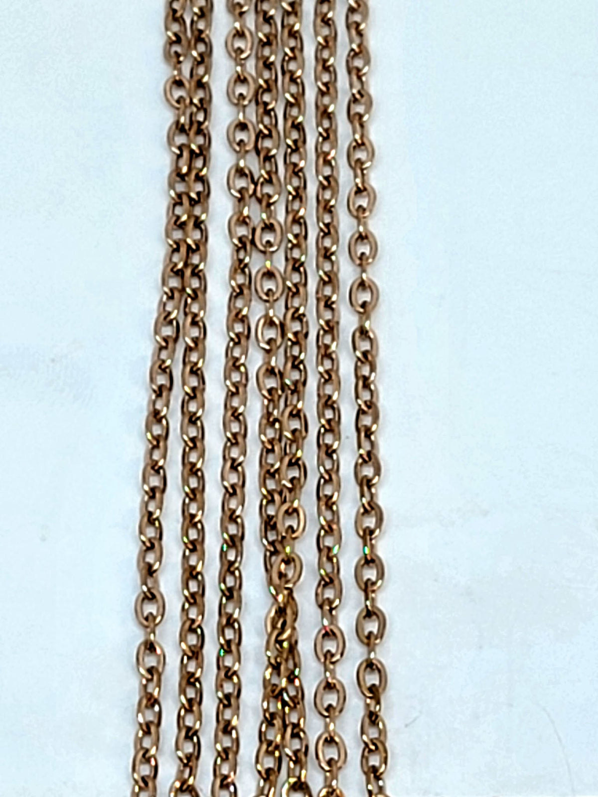 Hanging strands of 2mm rose gold stainless steel link chain against a white background