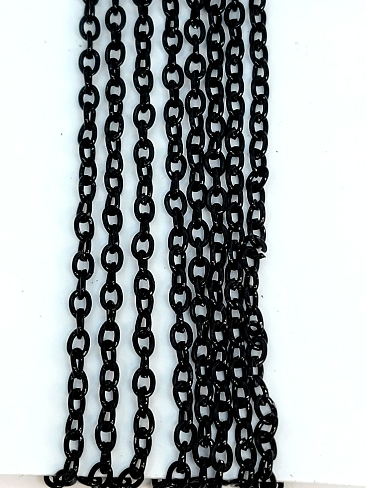 Hanging strands of 2 x 3mm black stainless steel link chain against a white background