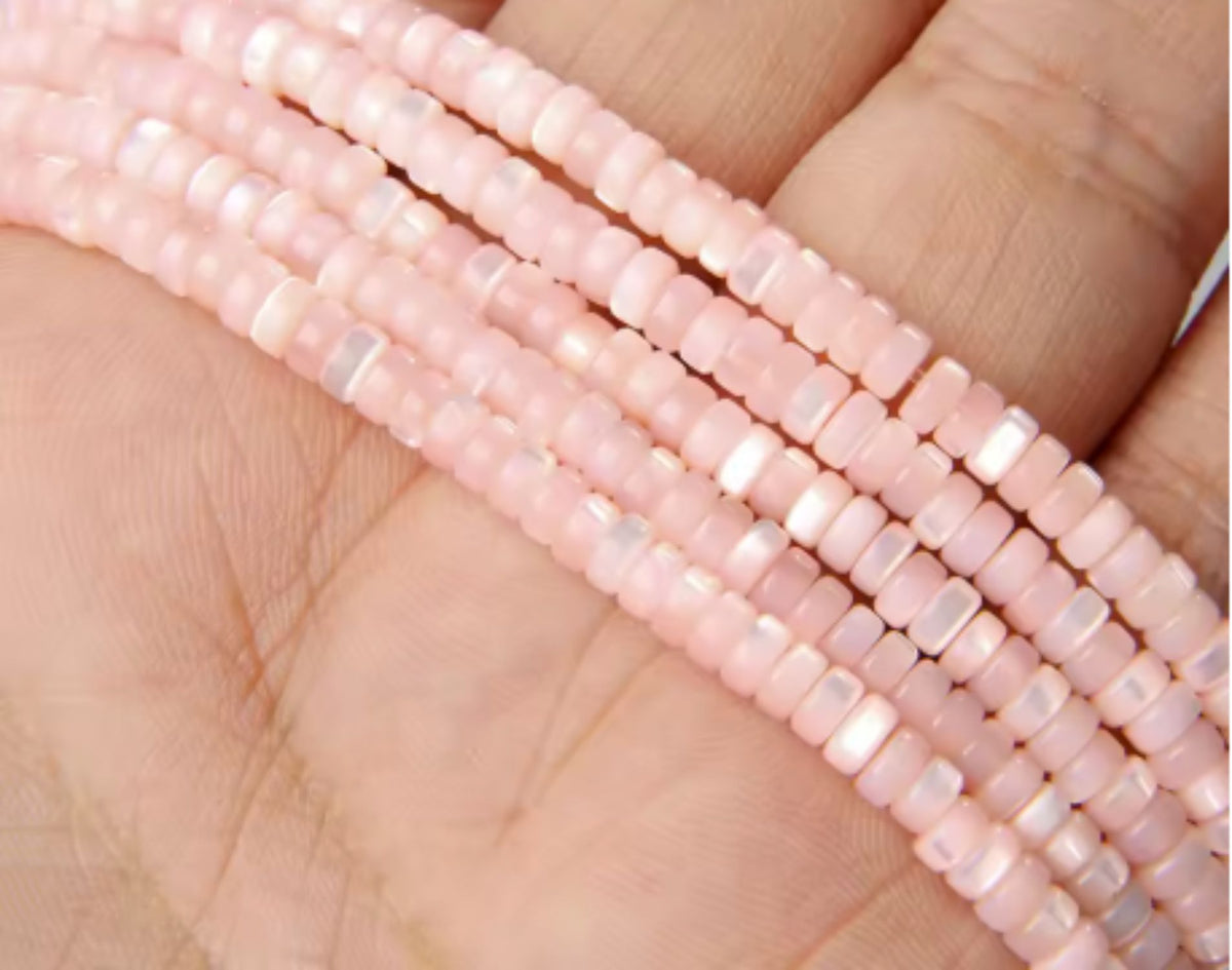Strands of pink 2 x 4mm mother of pearl disc beads held in a hand
