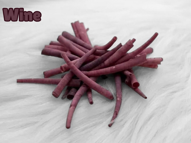 Pile of wine dyed smooth dentalium shells, about 1.5 to 2 inches long, on white faux fur