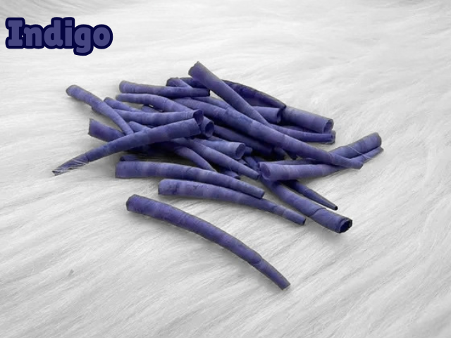 Pile of indigo dyed smooth dentalium shells, about 1.5 to 2 inches long, on white faux fur