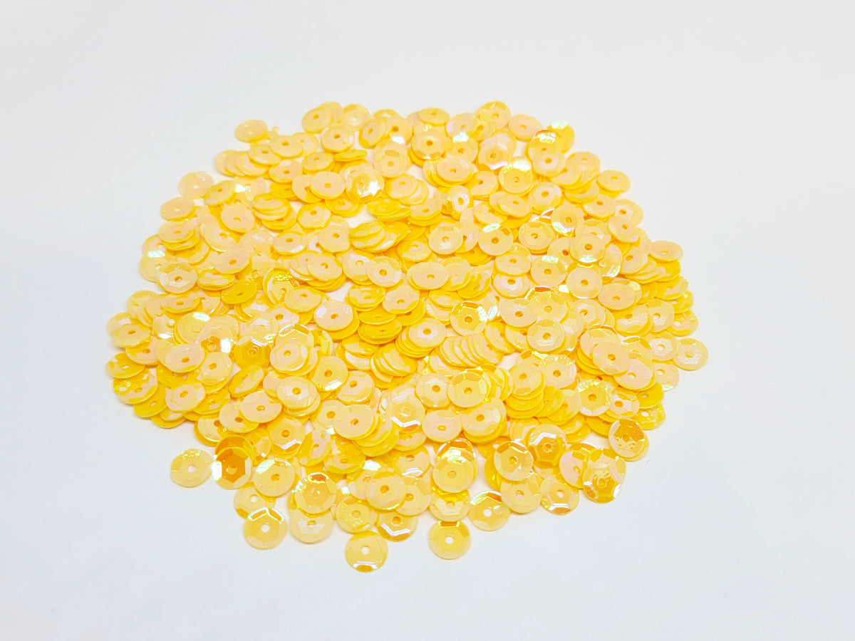 Pile of 6mm round dark yellow sequins with centre holes, on a white background
