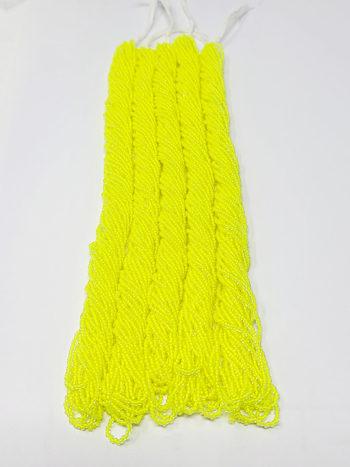 Five hanks of Preciosa 11/0 transparent neon yellow seed beads laid out on a white background