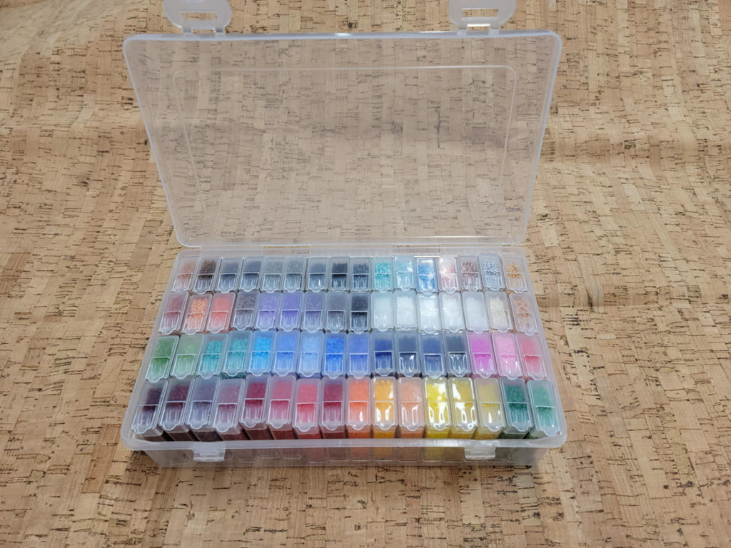 Clear plastic case of Preciosa 11/0 seed beads in 64 small tubes, open on a cork surface