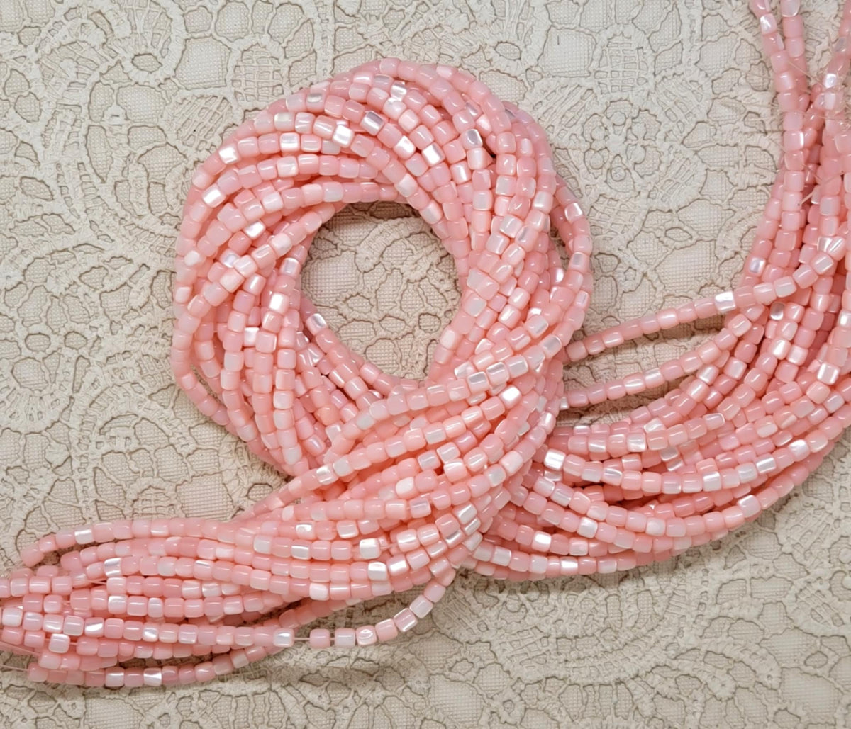 Pink 3mm mother of pearl cube bead strands draped over a hand