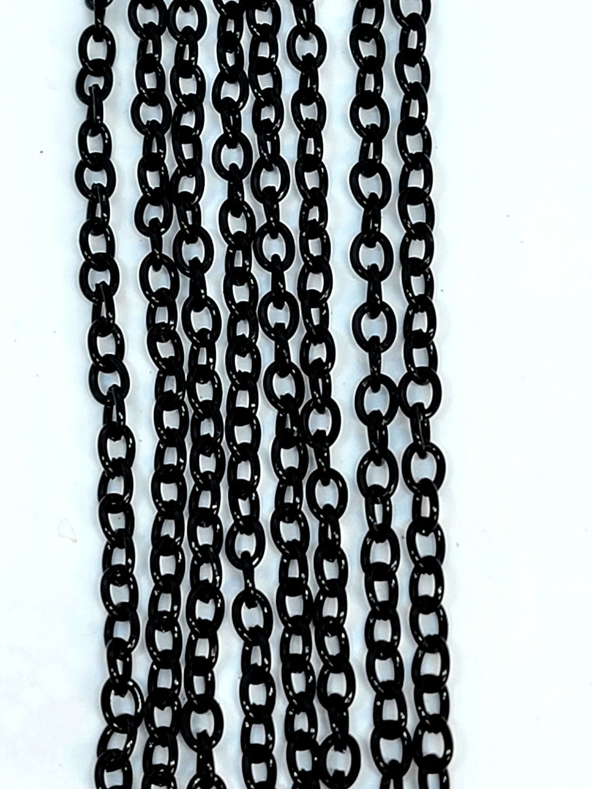 Hanging strands of 3 x 4mm black stainless steel link chain against a white background