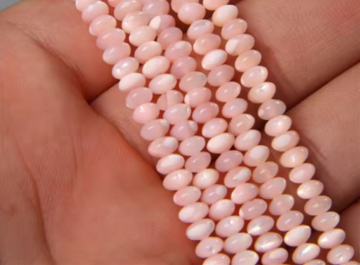 Strand of pink 3 x 5mm mother of pearl saucer beads held in a hand