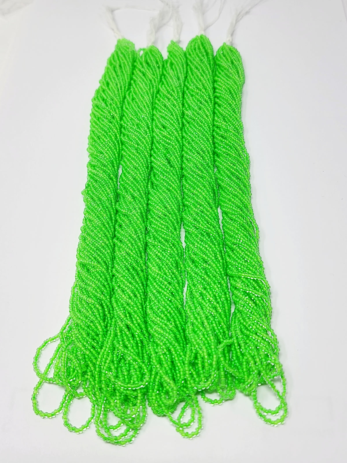 Five hanks of Preciosa 11/0 transparent neon green seed beads laid out on a white background