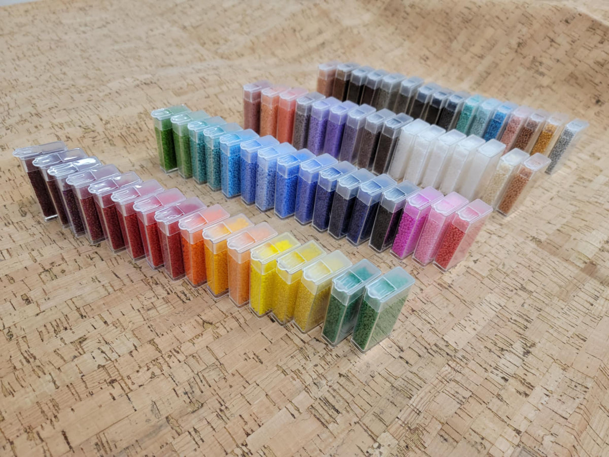 Rows of seed bead tubes from the variety box arranged by colour, from reds and yellows to blues and greys
