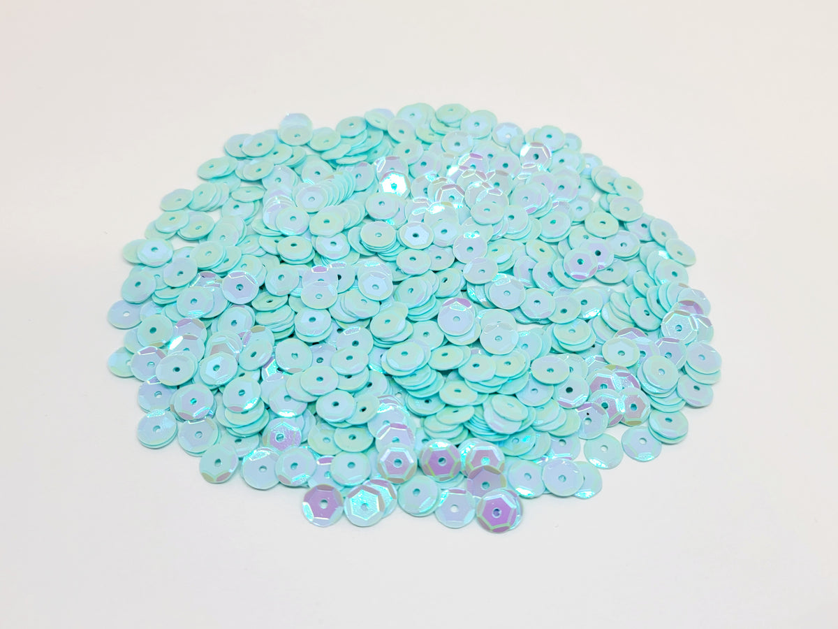 Pile of 6mm round seafoam sequins with centre holes, on a white background