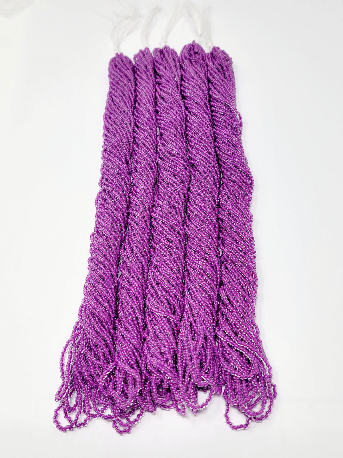 Five hanks of Preciosa 11/0 transparent neon purple seed beads laid out on a white background