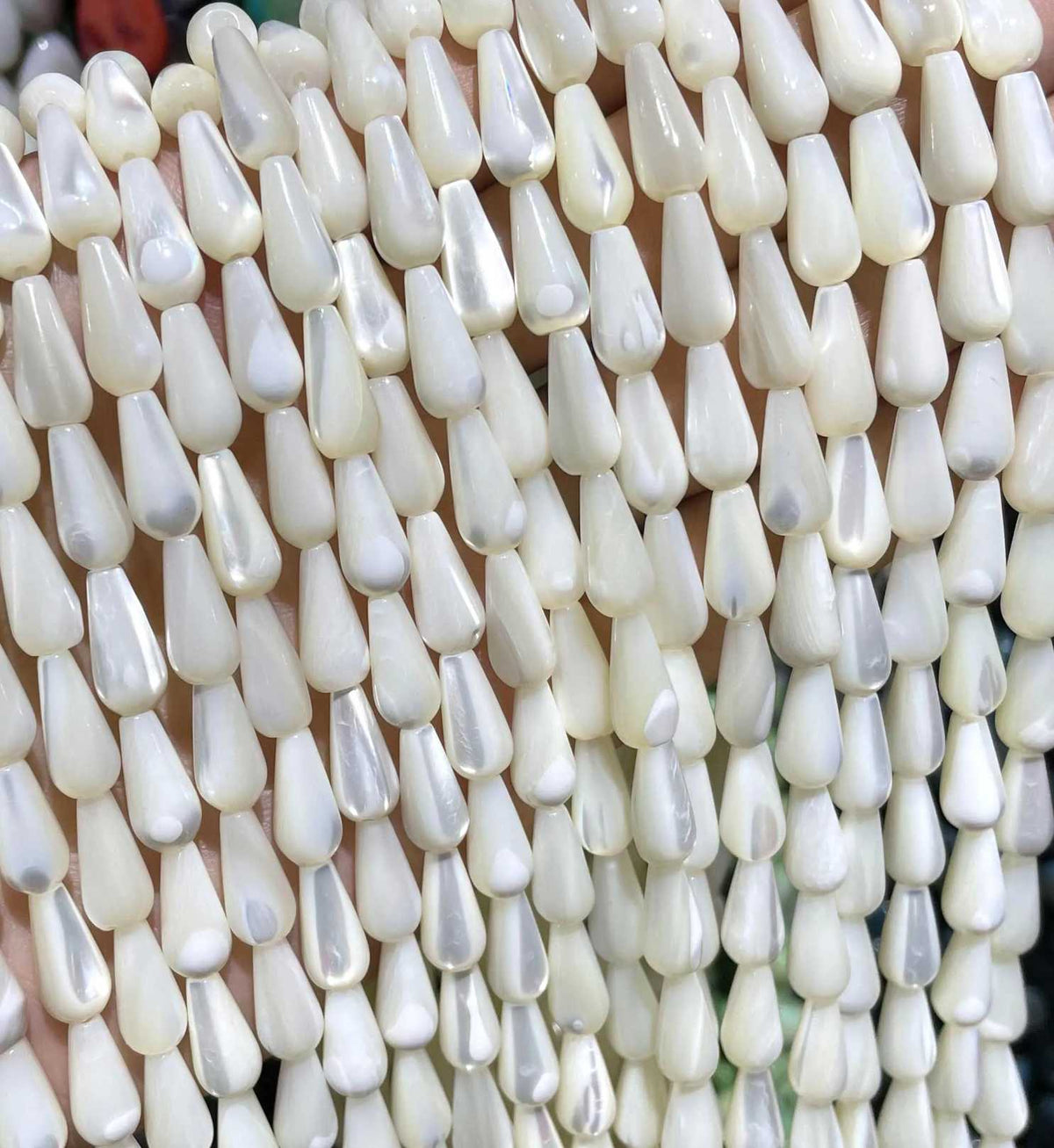 Rows of white 5 x 11mm mother of pearl drop bead strands, laid side by side