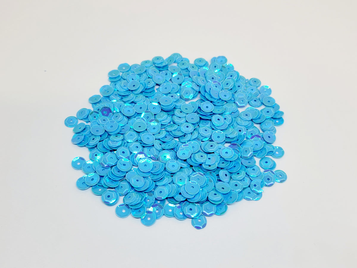 Pile of 6mm round blue sequins with centre holes, on a white background