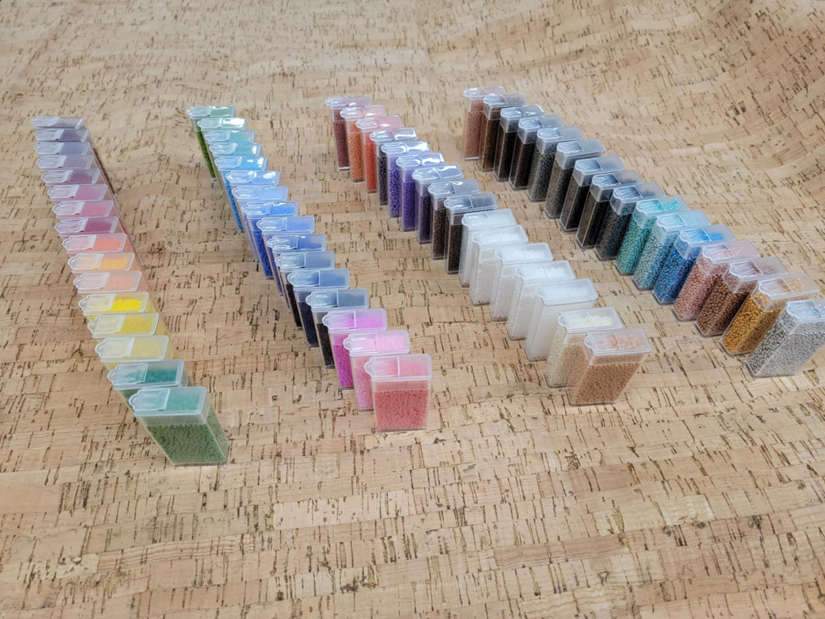 Bead tubes from the variety box laid out in four long lines on cork, grouped from light to dark shades
