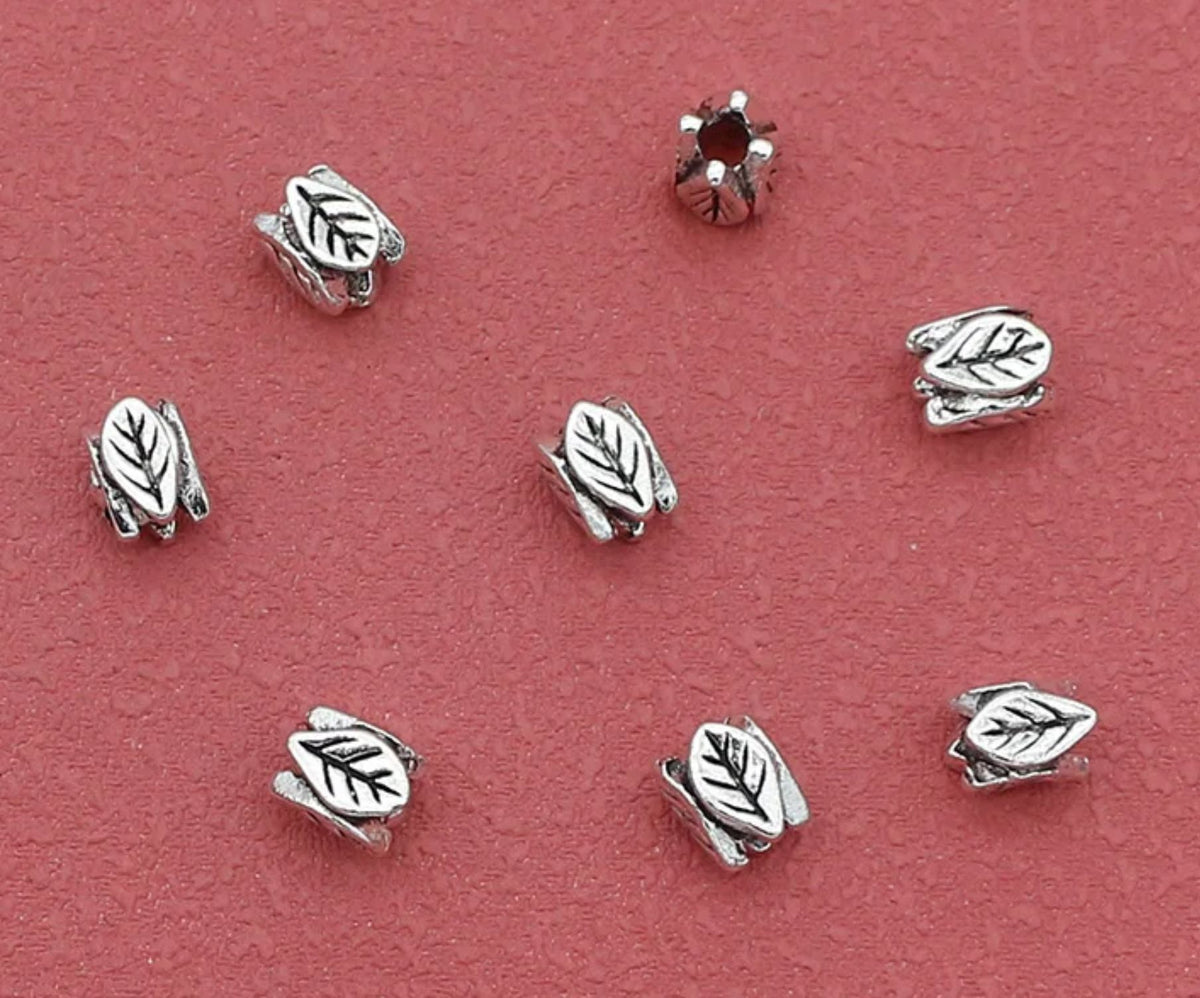 Silver-tone 6 x 7mm leaf spacer beads on a red background, seen from above