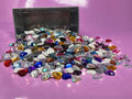 Pile of faceted heart gem cabochons (cabs) in mixed colours spilling from a metal tin