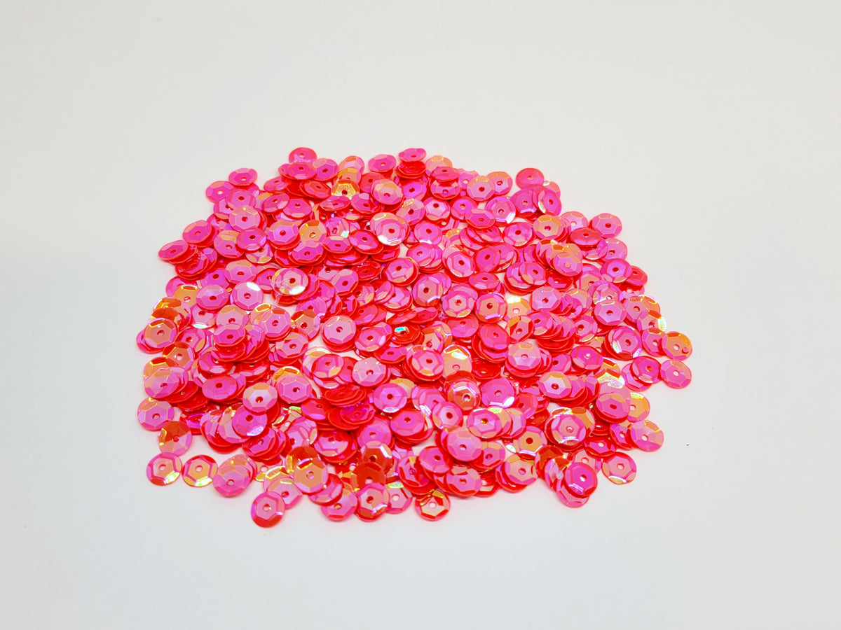 Pile of 6mm round flamingo sequins with centre holes, on a white background