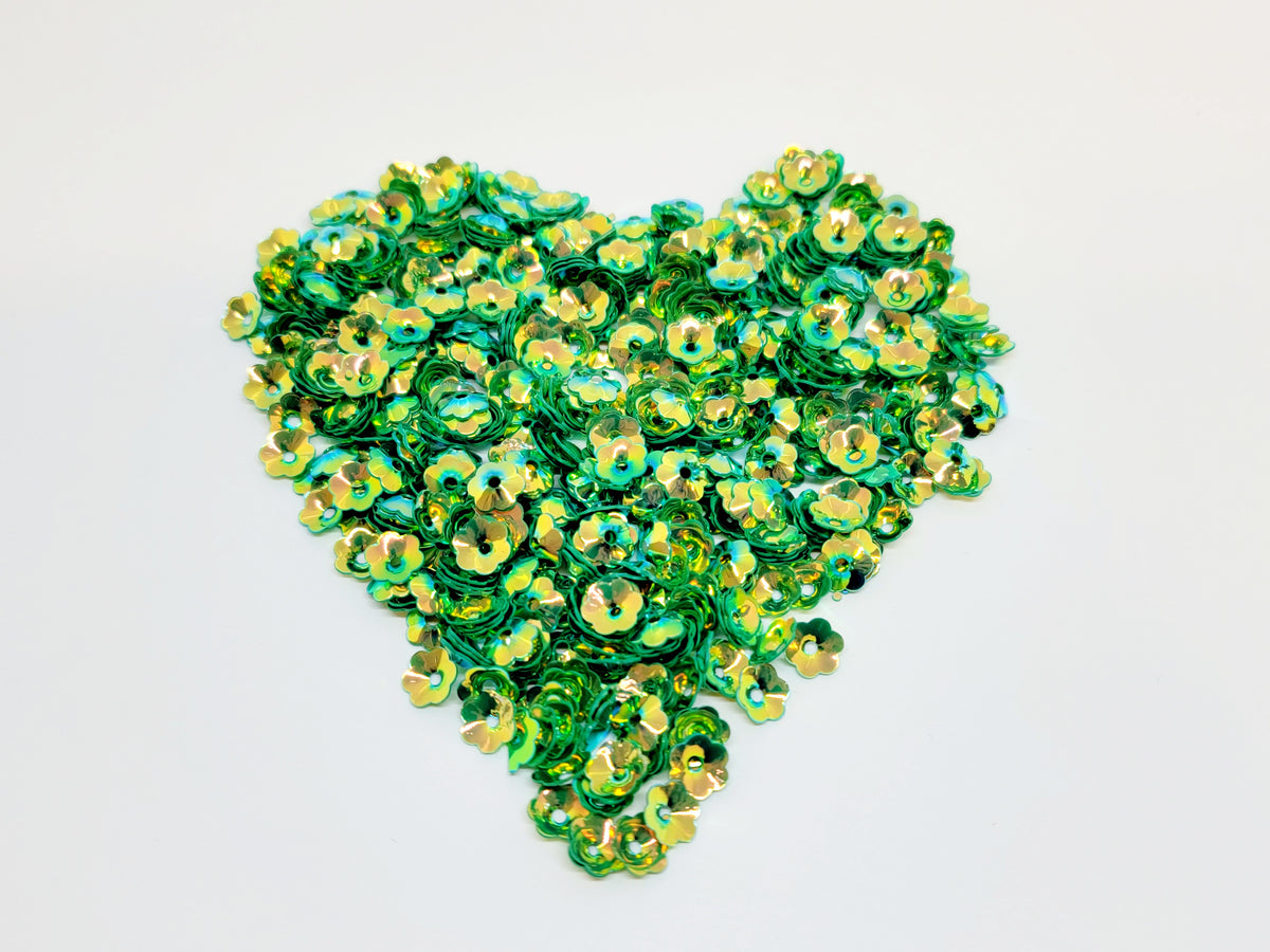 Heart-shaped pile of 6mm iridescent flower sequins in green on a white background