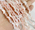 Strand of pink mother of pearl crescent moon beads, 8 x 11mm, held in a hand